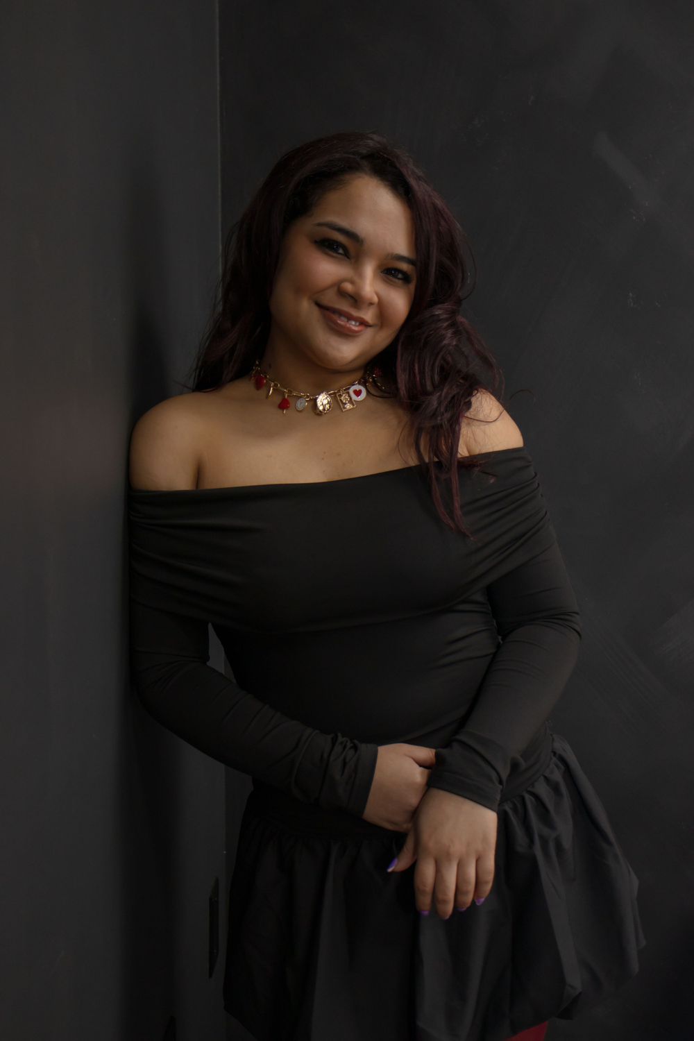Girl wearing a black dress, leaning against a black wall.