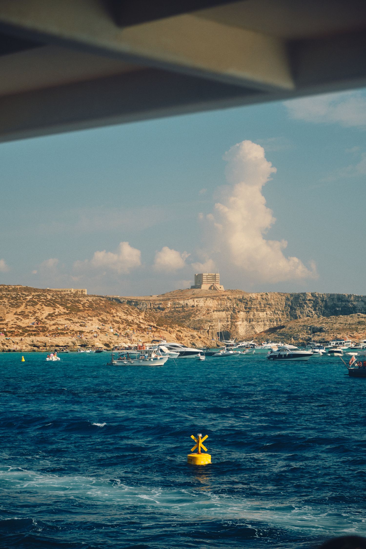 Dramatic cloudscape over Malta's rocky coastline with boats dotting the azure Mediterranean waters.