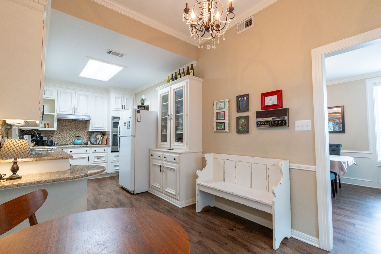 Bright kitchen and dining space with white wainscoting, beige walls, chandelier, and hardwood flooring.