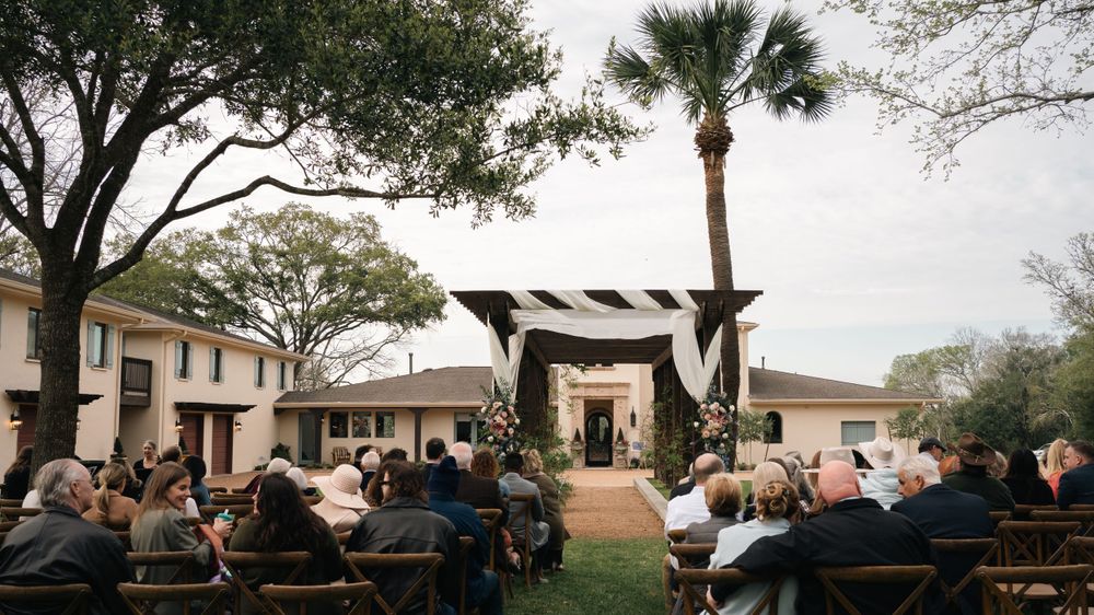 Guests seated at outdoor wedding ceremony venue with palm trees and rustic wooden chuppah in Florida.
