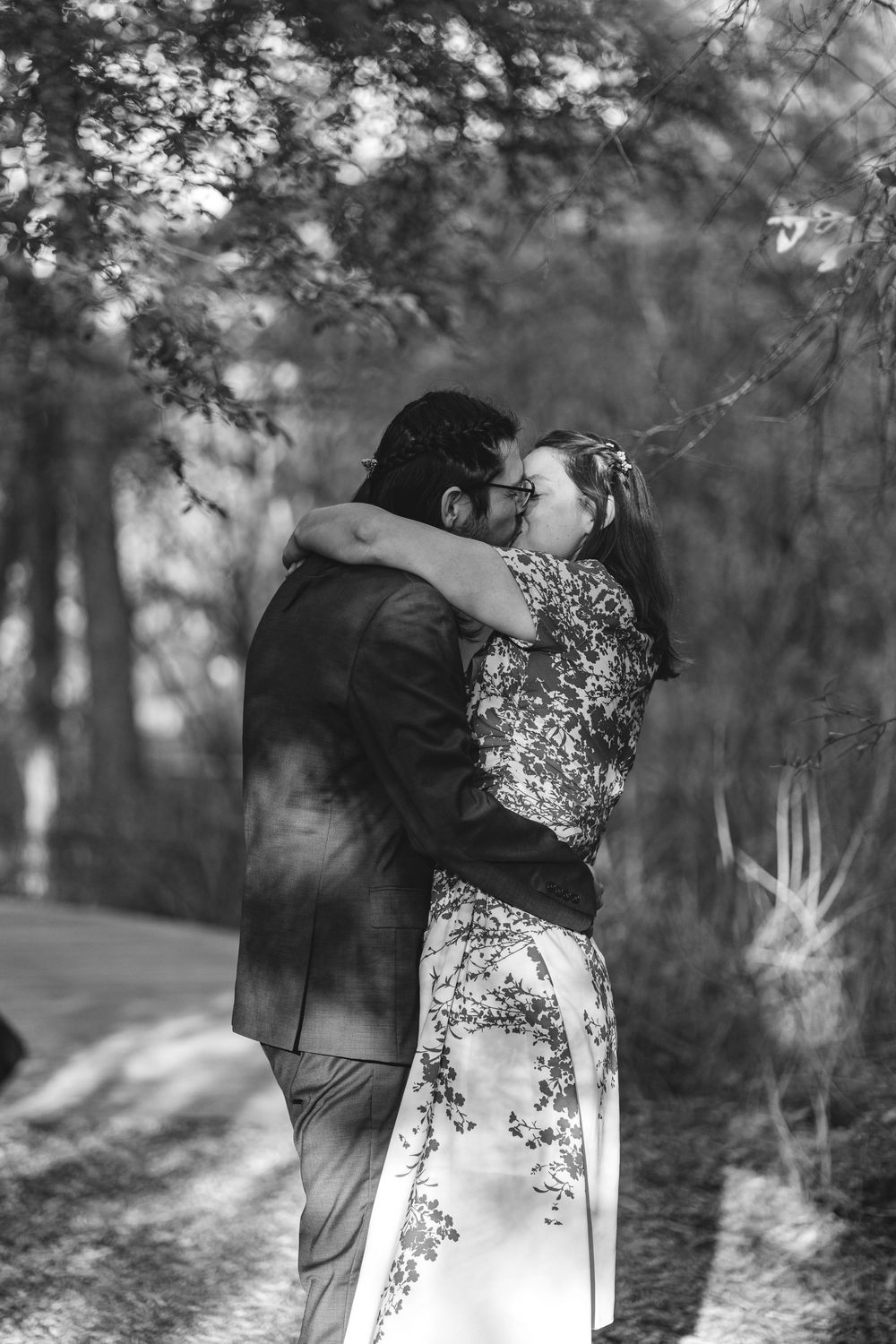 A couple embraces in a romantic dance pose among trees in a dreamy black and white forest setting.