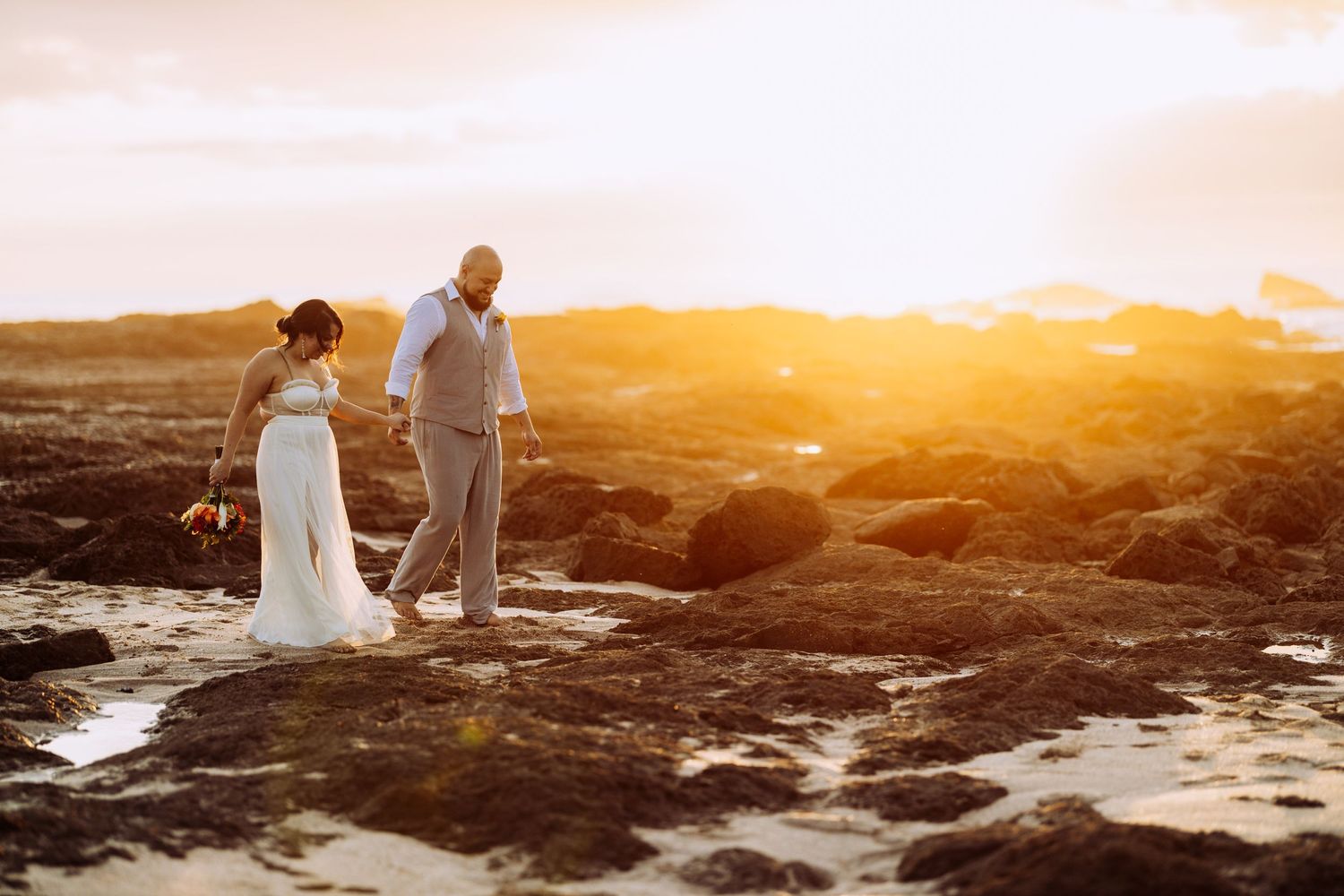 Couple walking on rocky coastline during golden hour sunset.