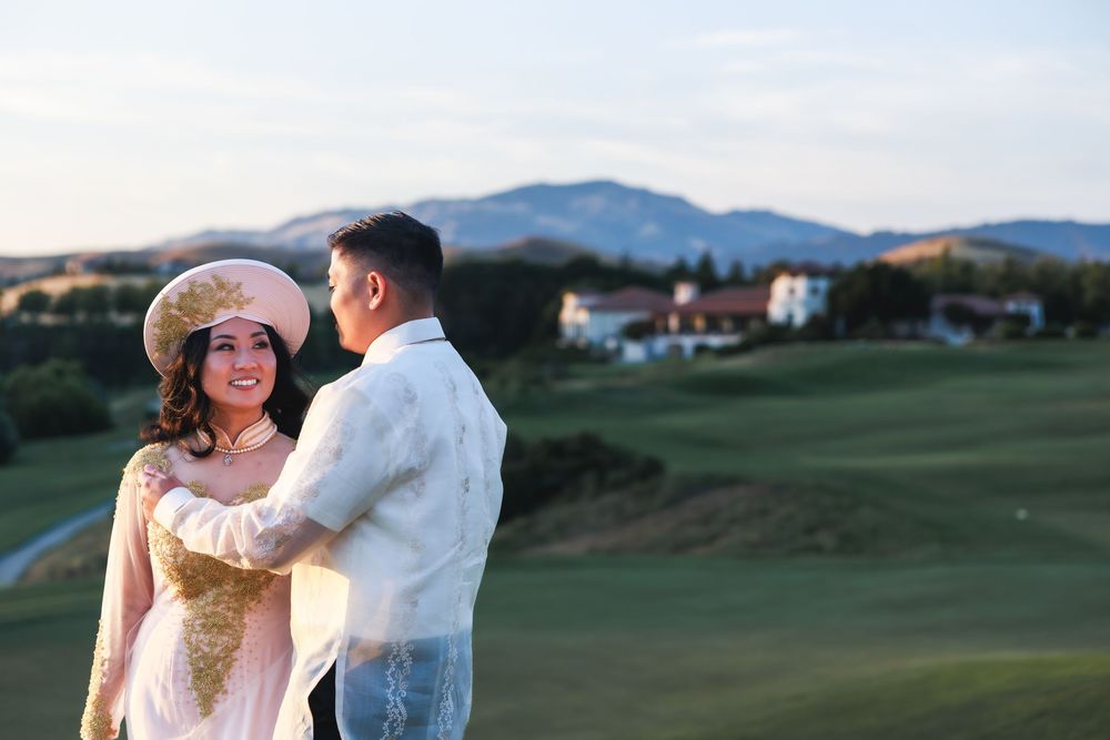 A couple embraces in a romantic moment on a golf course with mountains and greenery in the background.