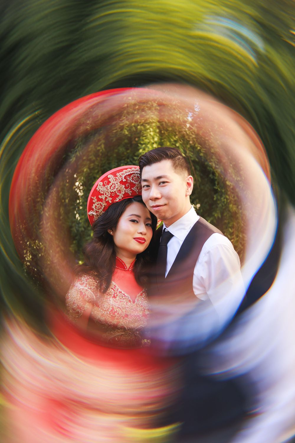 Swirling artistic wedding portrait with red and blue tones creating a dreamy vortex effect in an outdoor garden setting.