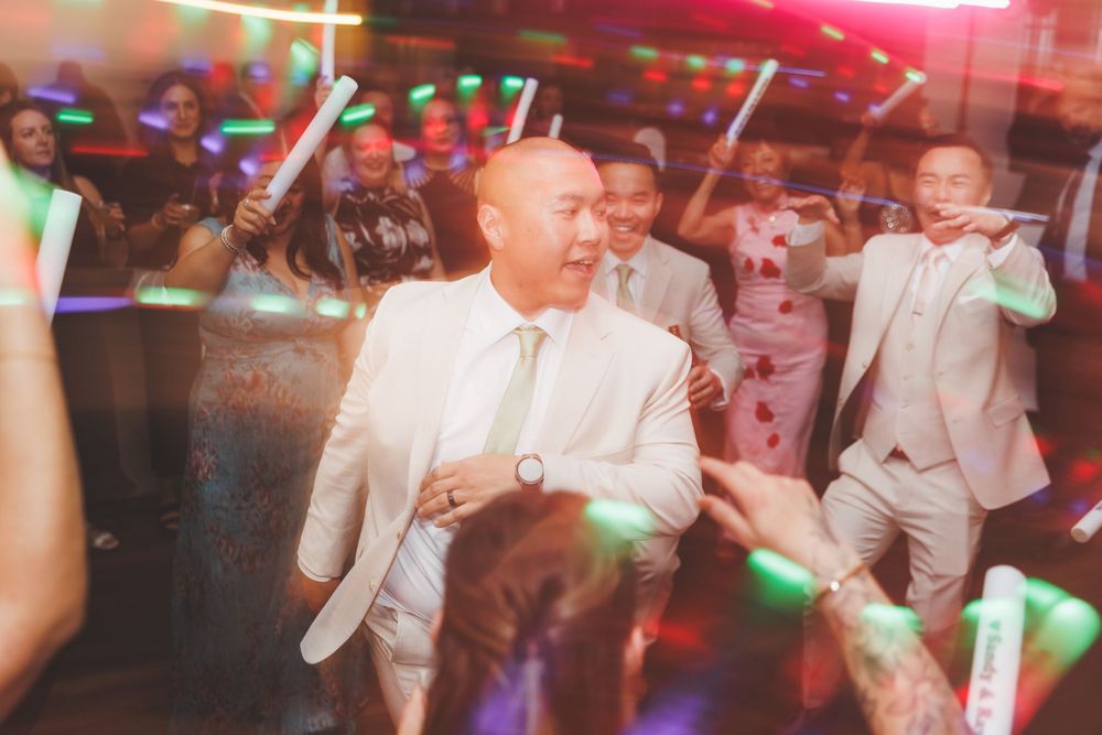 People dancing and celebrating at a wedding reception with colorful disco lights illuminating the dance floor.