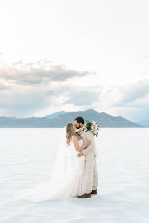 Romantic couple embracing on salt flats with mountain vista in background.
