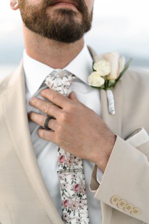 Groom's formal attire detail showing floral tie, boutonniere and wedding ring.