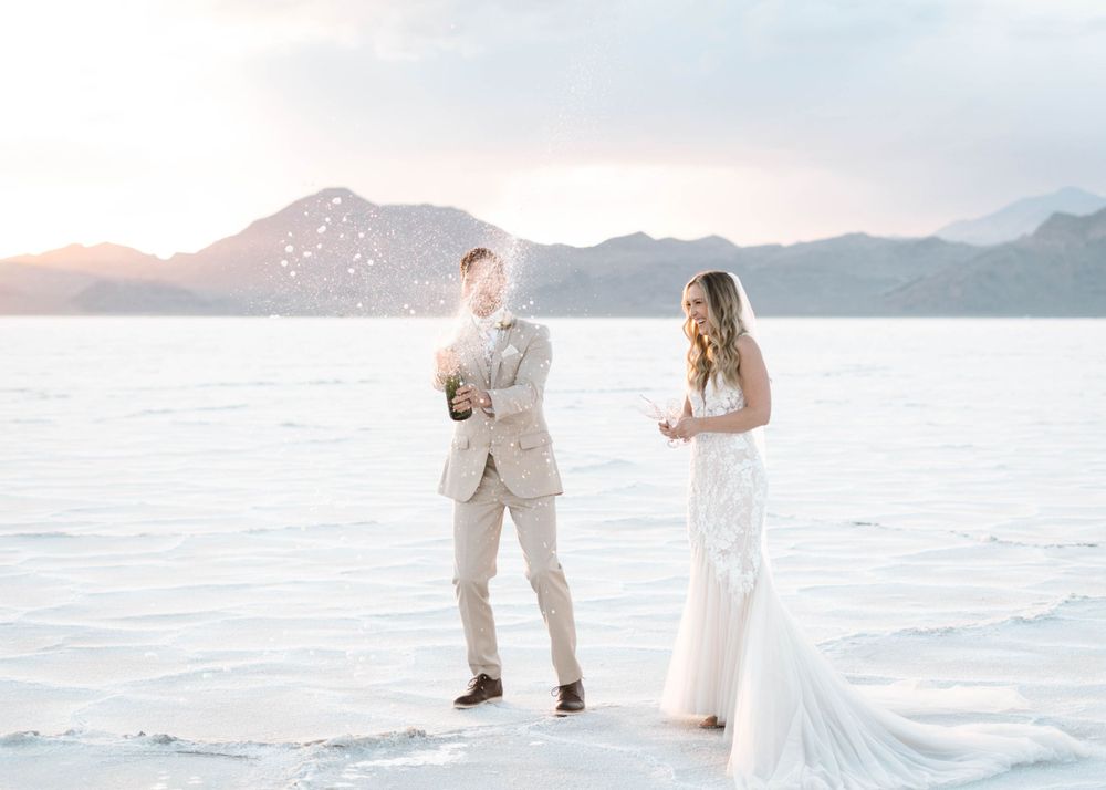 A romantic wedding couple poses at sunset on a white salt flat with mountains in the background.