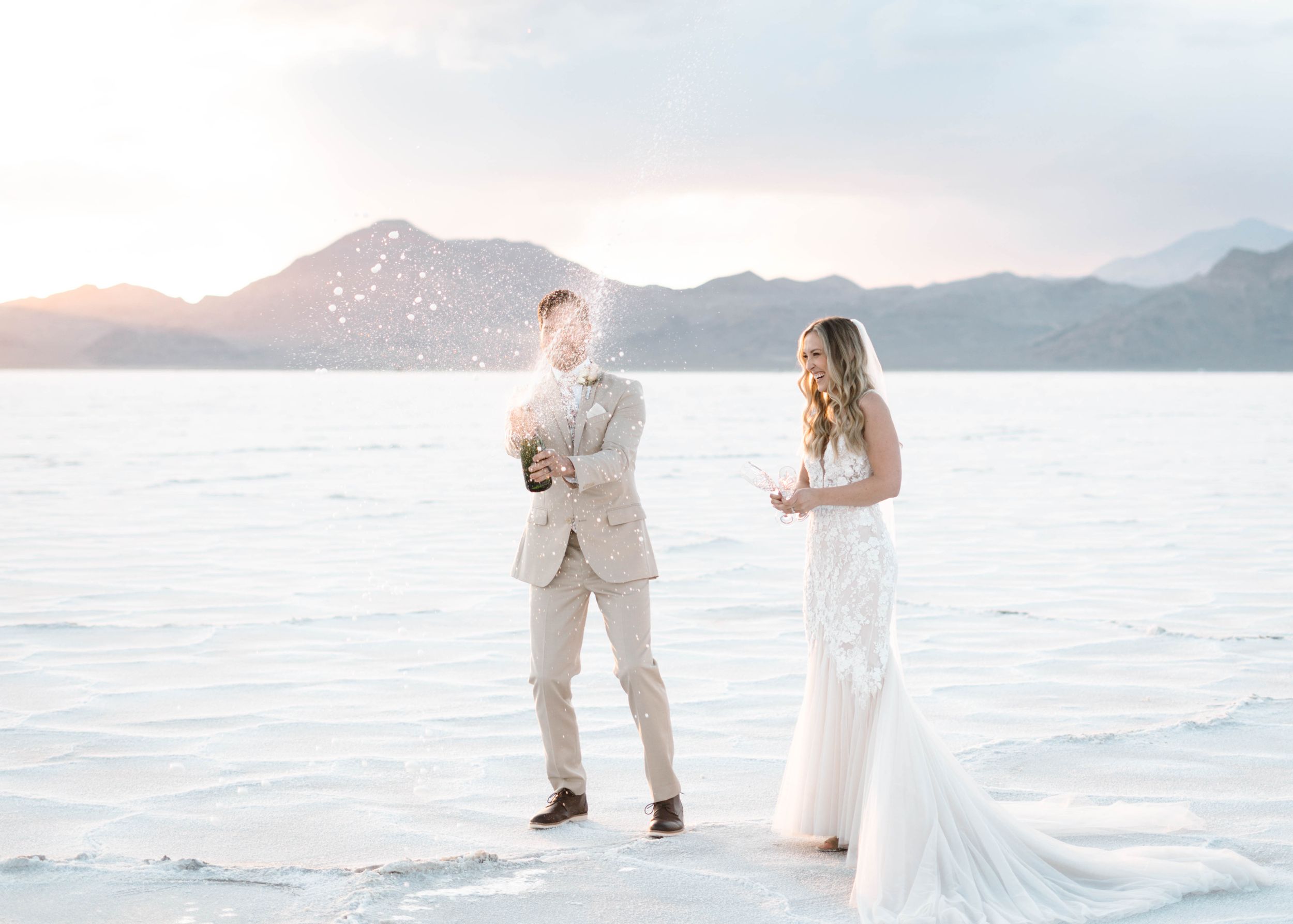 A romantic wedding couple poses at sunset on a white salt flat with mountains in the background.