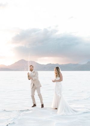 Newlyweds celebrate joyfully on salt flats with mountains during golden hour.