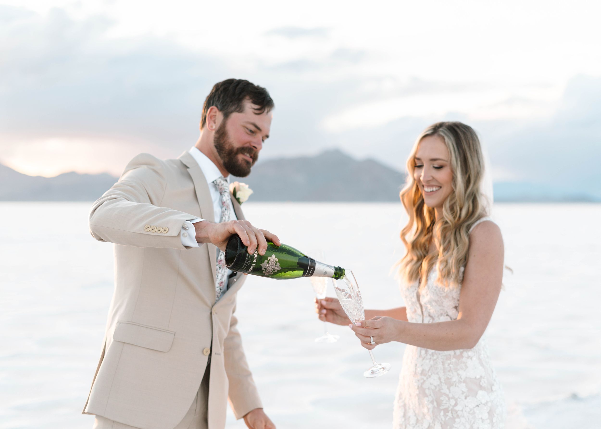 Newlyweds celebrating with champagne on salt flats at sunset.
