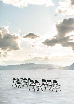 Empty folding chairs arranged for outdoor wedding ceremony on salt flats with mountain backdrop.