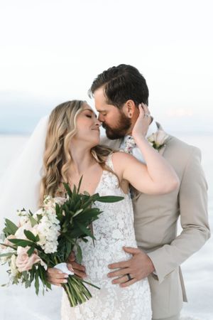 Romantic wedding portrait with bride holding white bouquet against scenic mountain backdrop.