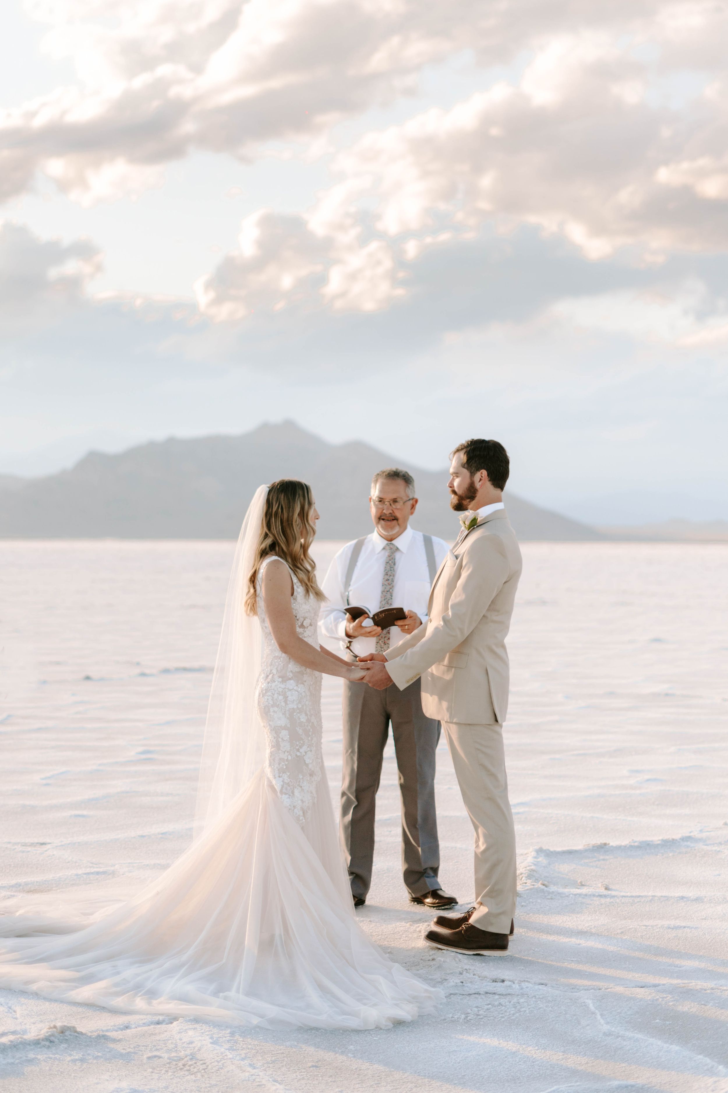 Wedding ceremony taking place on white salt flats with mountains and cloudy sky in the background.