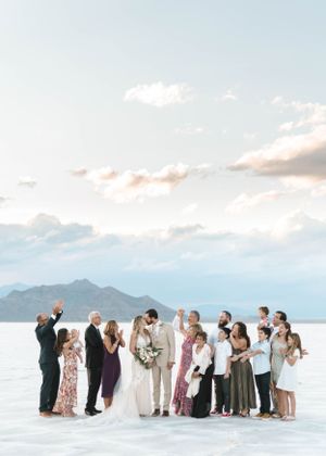 Wedding party group photo on salt flats with mountains and sunset sky in background.