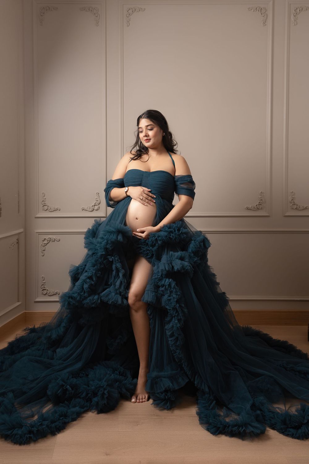 Luxurious teal maternity gown with dramatic tulle details in classic studio setting.