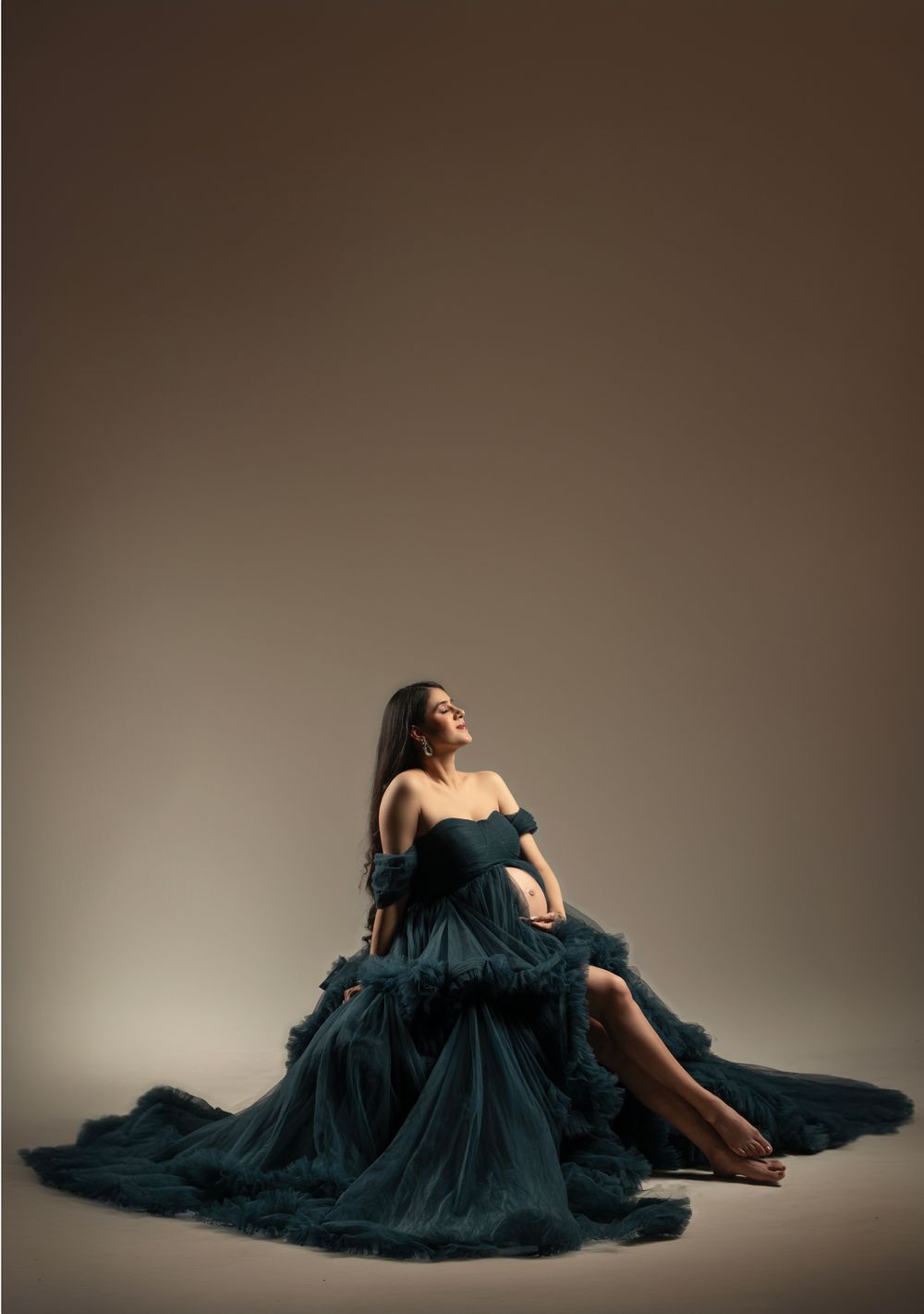 Artistic maternity portrait featuring elegant dark teal flowing dress against neutral backdrop.