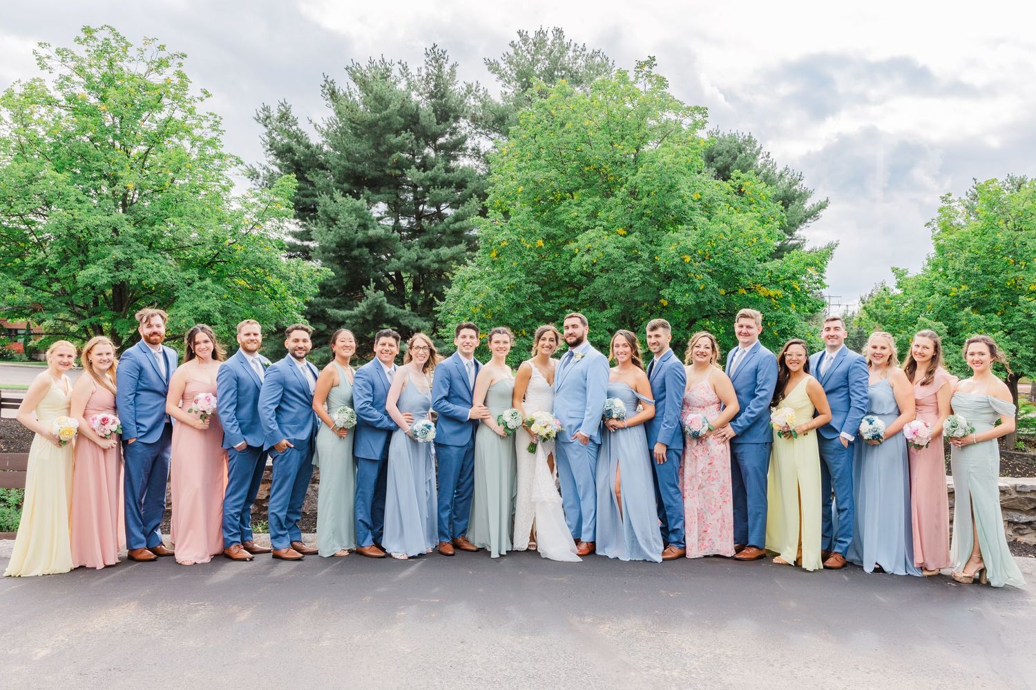 Wedding party wearing coordinated blue and pink dresses and suits posing together outdoors.