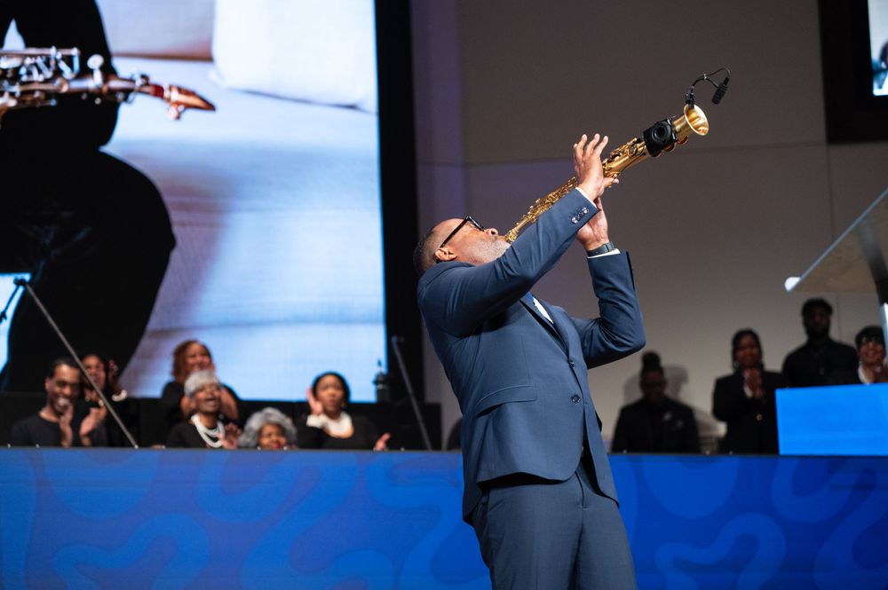 Performers on stage at a church or concert venue with dramatic blue lighting effects.
