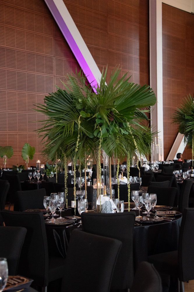 Tropical palm frond decorations accent formal dining tables with black linens and ambient lighting.