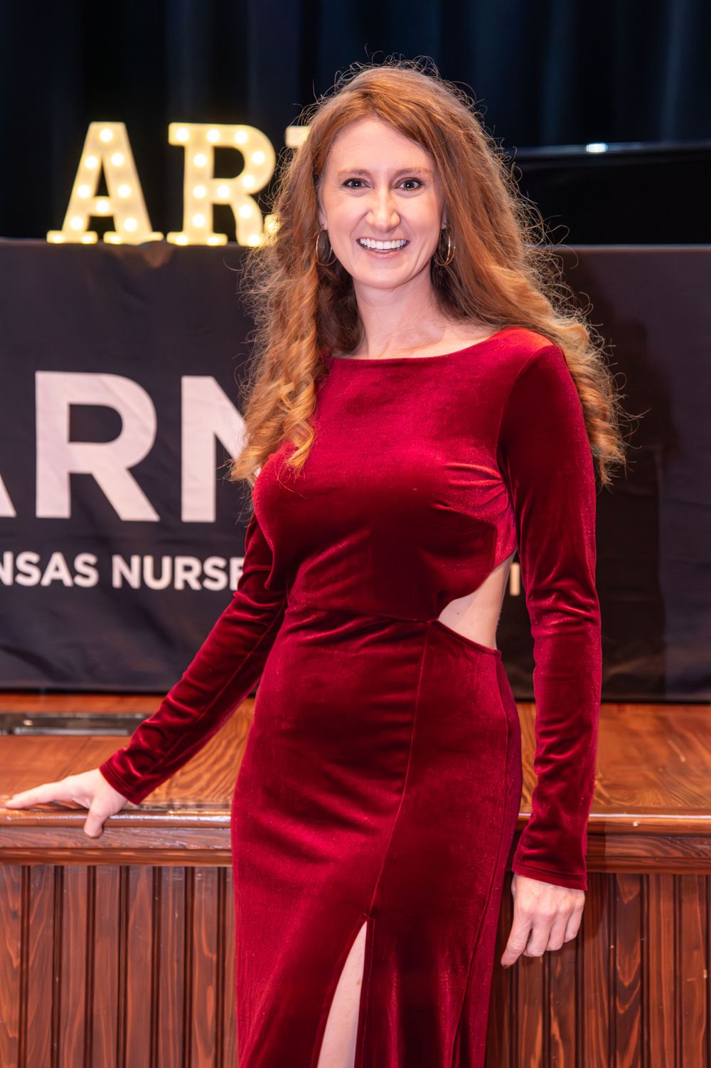 A person in a red velvet dress poses on stage during a formal event.