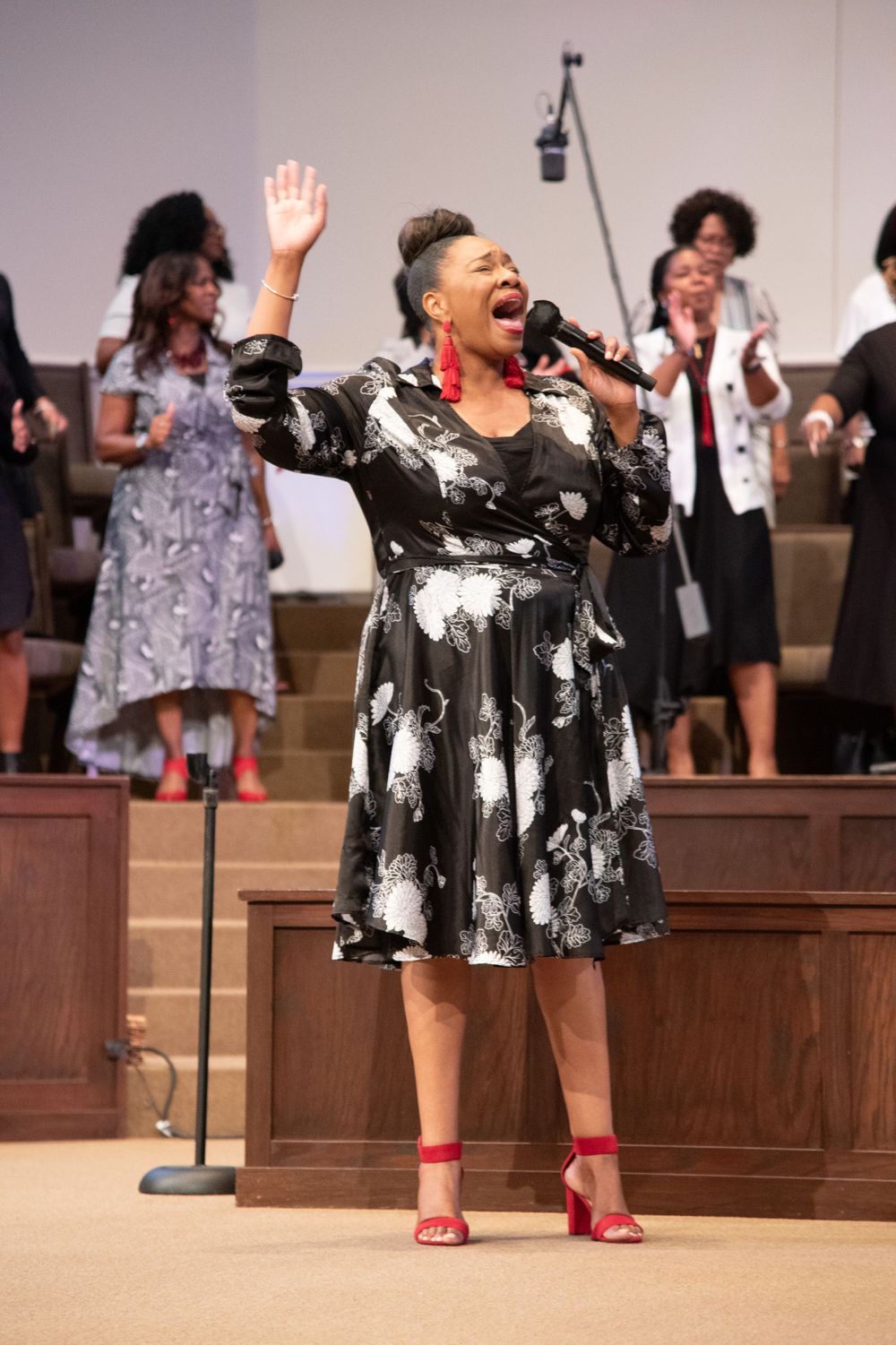 Performer in black and white patterned dress singing passionately on stage.