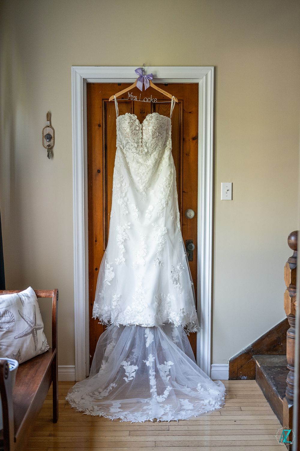 Elegant white lace wedding dress hanging on wooden door with long train visible.