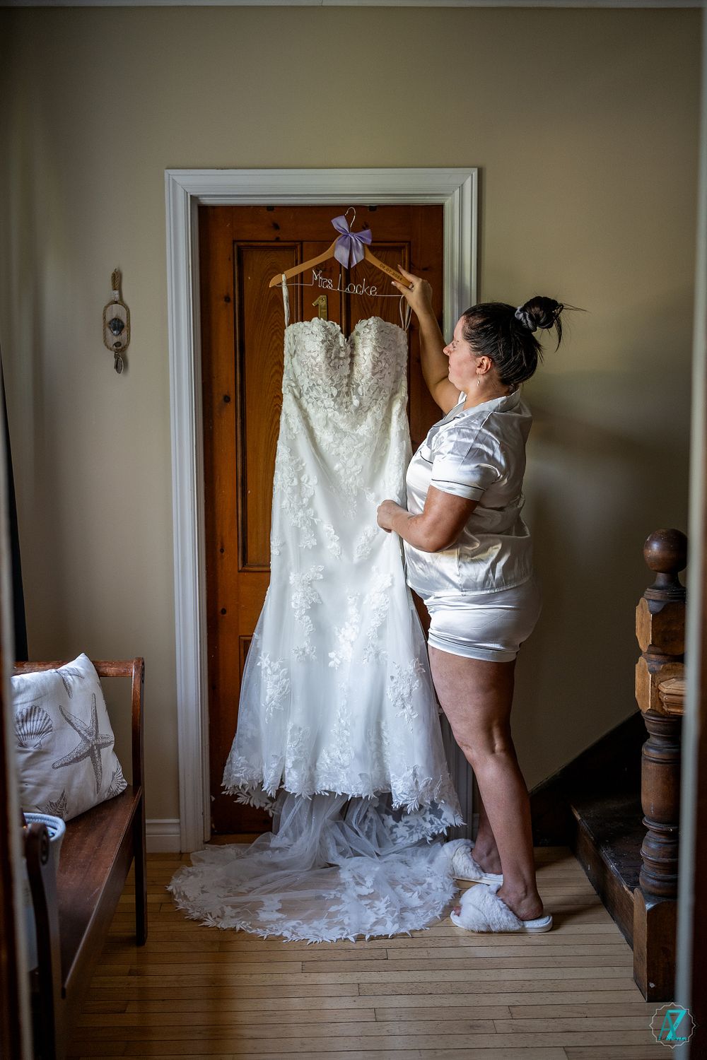 A white lace wedding dress with train hanging on wooden door while someone in casual attire admires it.