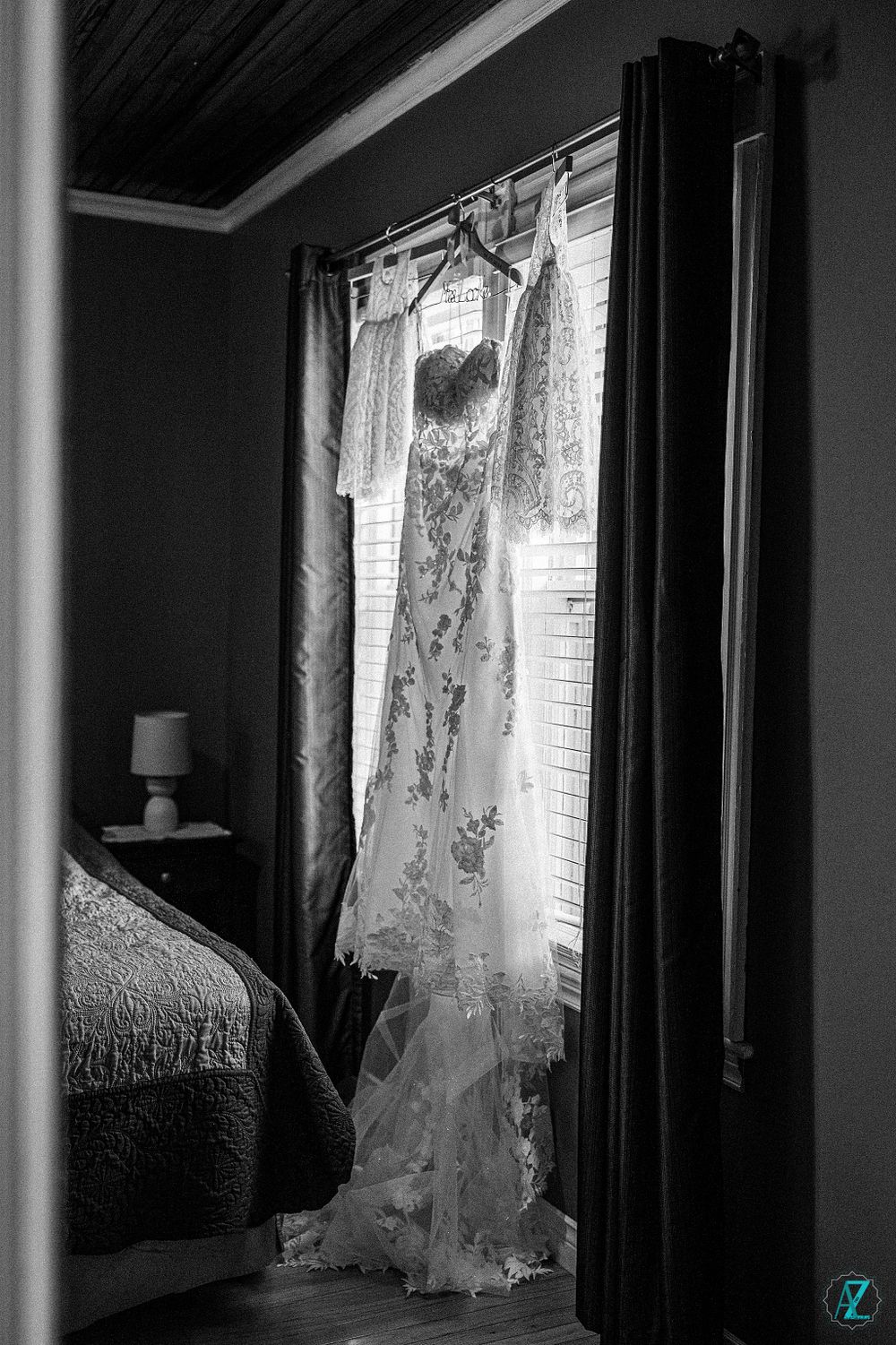 Black and white photo of a wedding dress hanging in front of a window with natural light.