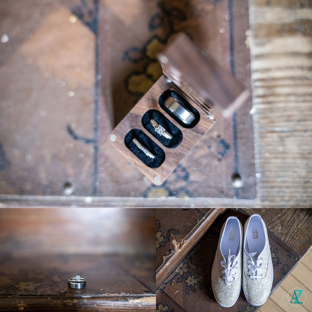 Wedding accessories including rings and white shoes arranged on rustic wooden surface.