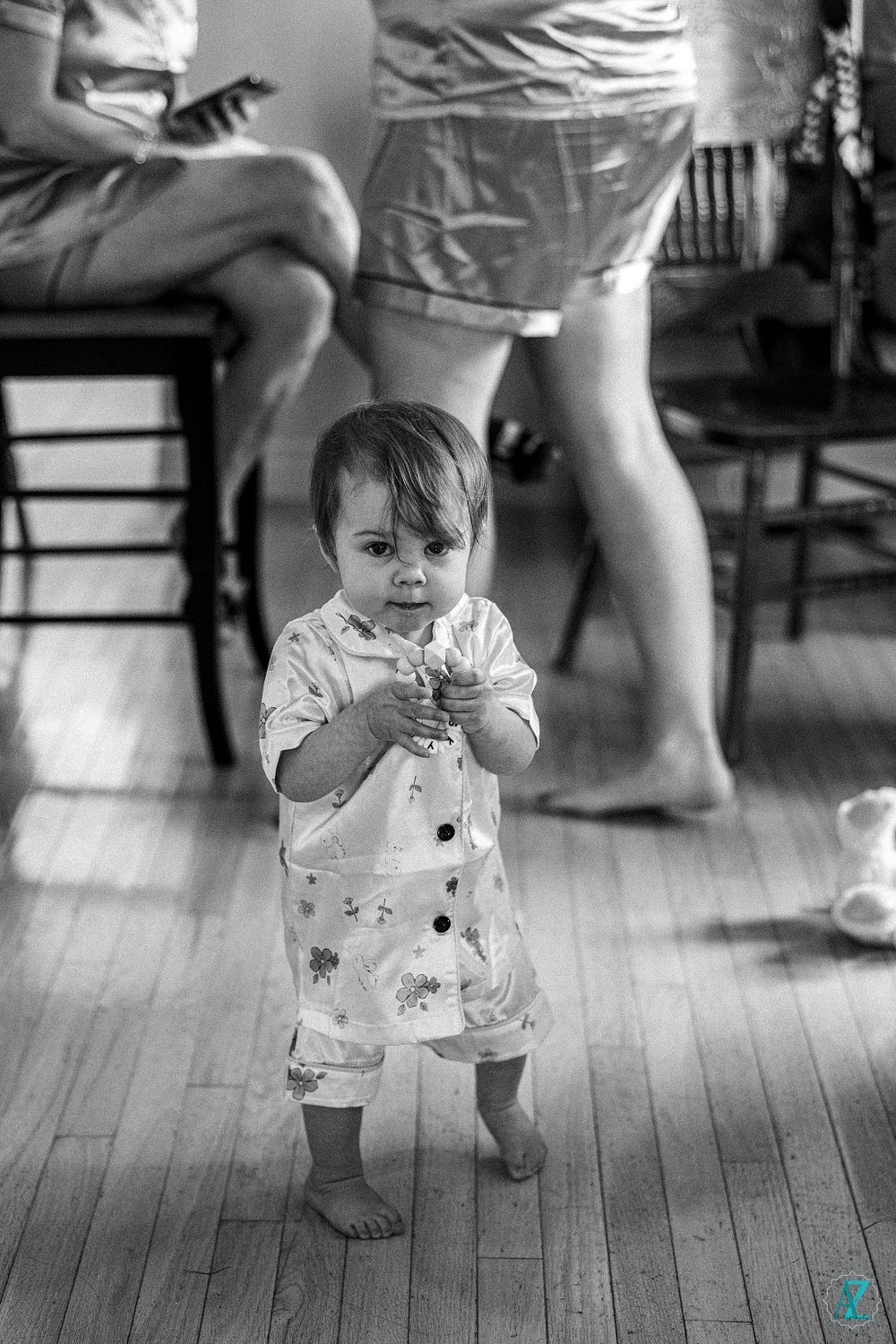 A toddler standing barefoot on hardwood floors wearing a patterned outfit.