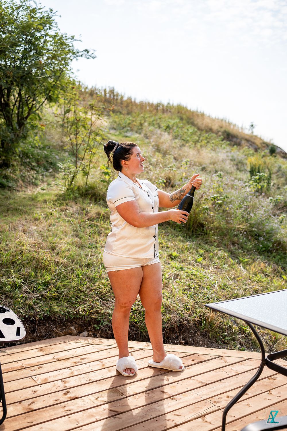 A person standing on a wooden deck preparing to open a bottle of champagne outdoors.