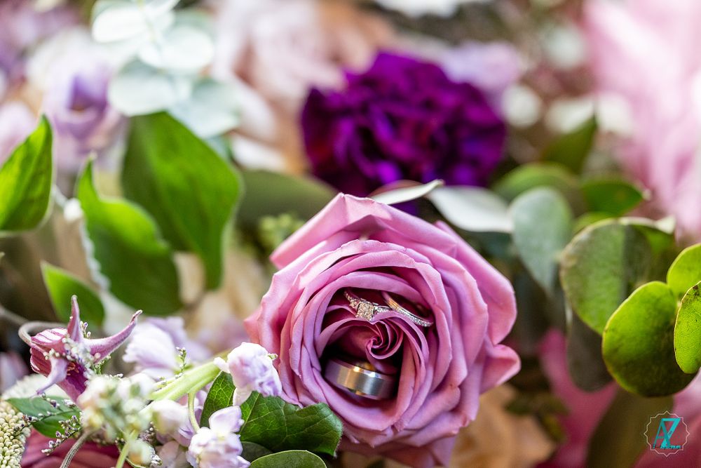 Close-up of a pink rose with purple flowers and green foliage in a bouquet arrangement.