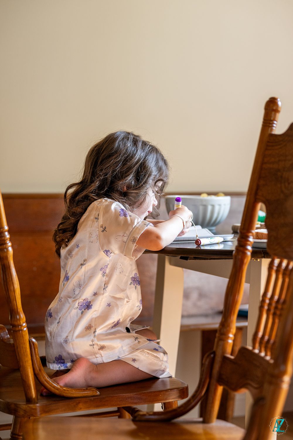 A child in floral dress sitting at dining table writing or drawing.
