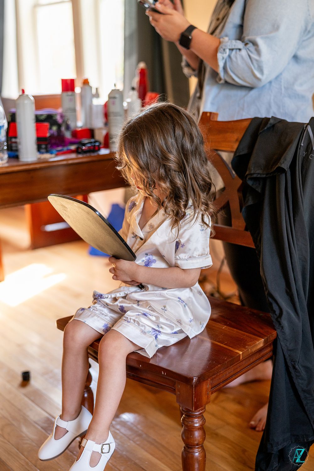 Young attendee looking at tablet while getting styled in a sunny preparation room.