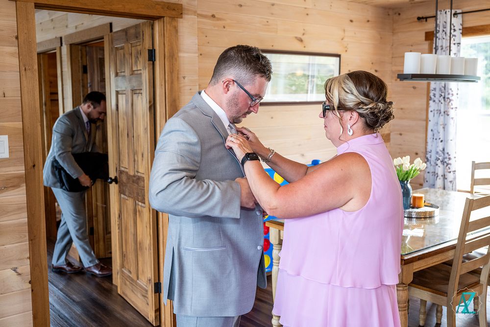Final adjustments being made to wedding attire in a rustic wooden cabin setting.