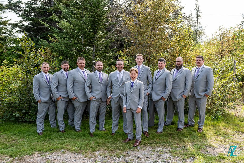 Wedding party in matching grey suits poses outdoors against a natural backdrop.