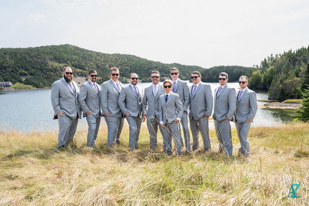 Groomsmen in matching grey suits lined up along a scenic lakeside vista.