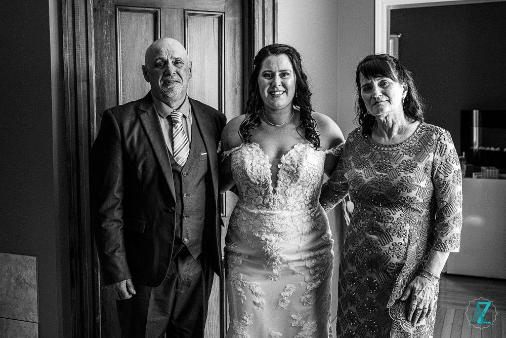 Wedding party portrait in formal attire against dark interior backdrop.