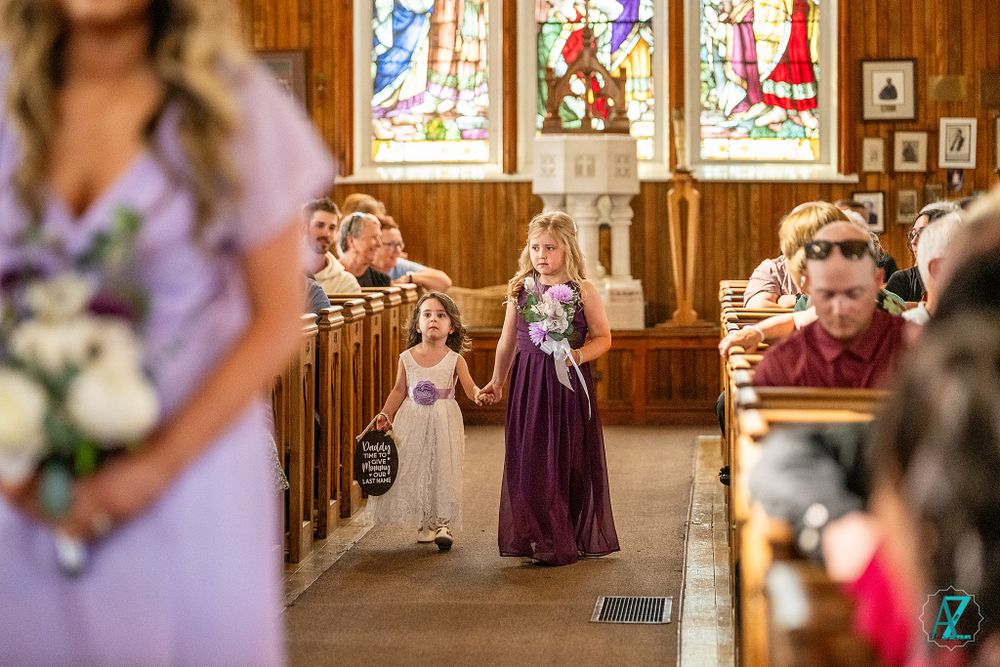 Wedding processional in church with stained glass windows and wooden pews.