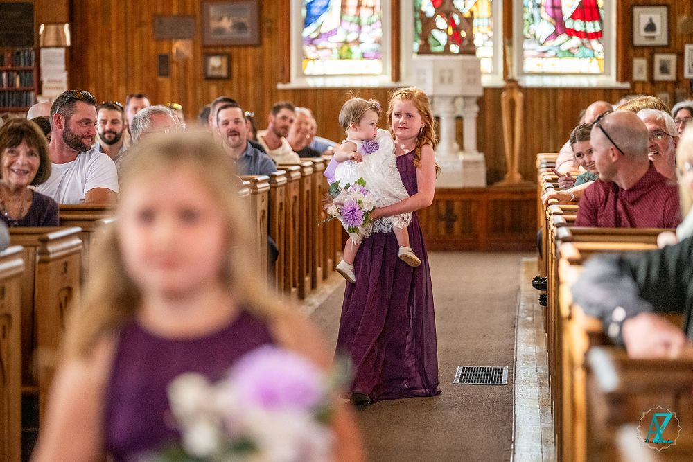 Processional walking down church aisle while guests watch from wooden pews.