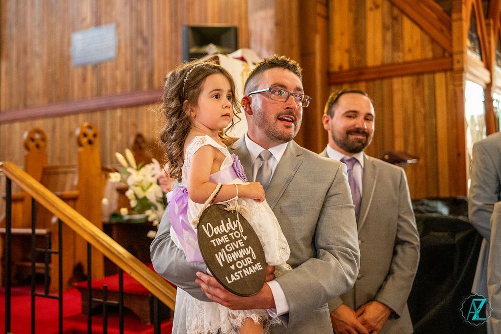 Wedding party members stand at altar in wood-paneled church with red carpet.