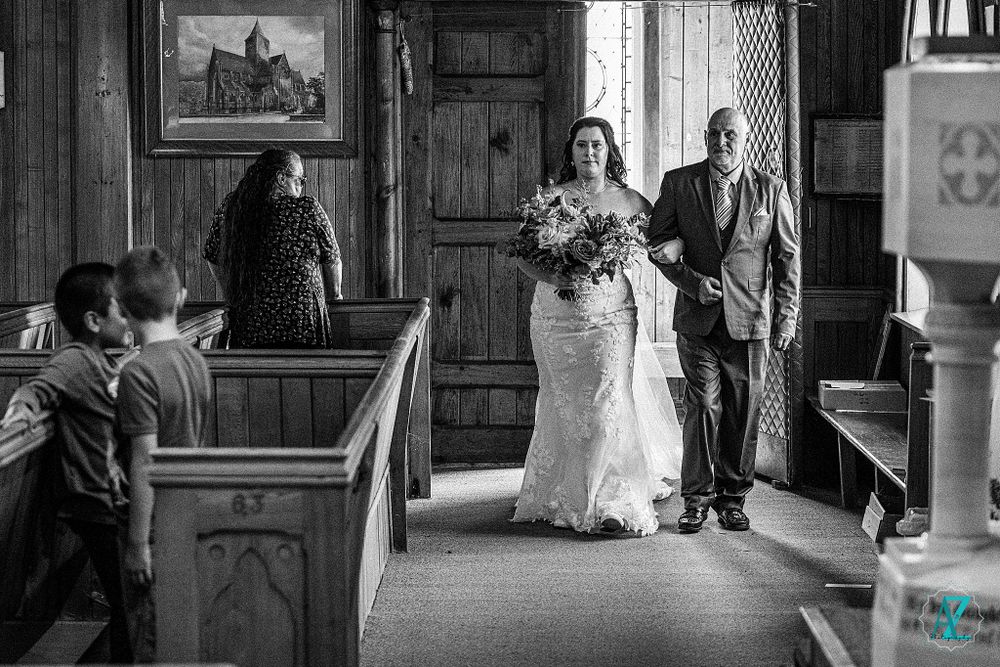 Black and white image of a wedding processional walking up the wooden aisle of a traditional church.