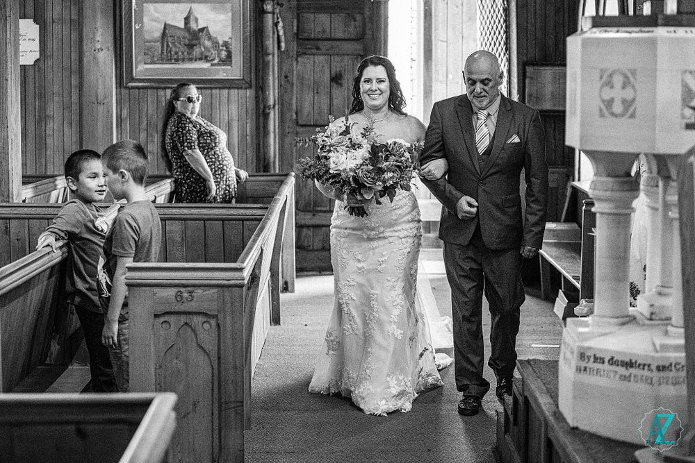 Wedding party members walking through a church with wooden pews and traditional decor.