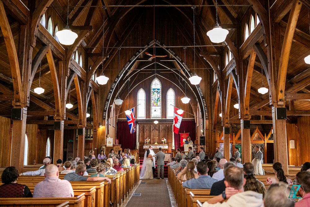 Wide view of wedding ceremony in historic church with vaulted wooden ceiling and stained glass windows.