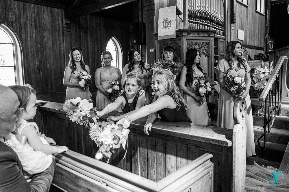 Wedding party members gather in traditional wooden church pews during a ceremony.