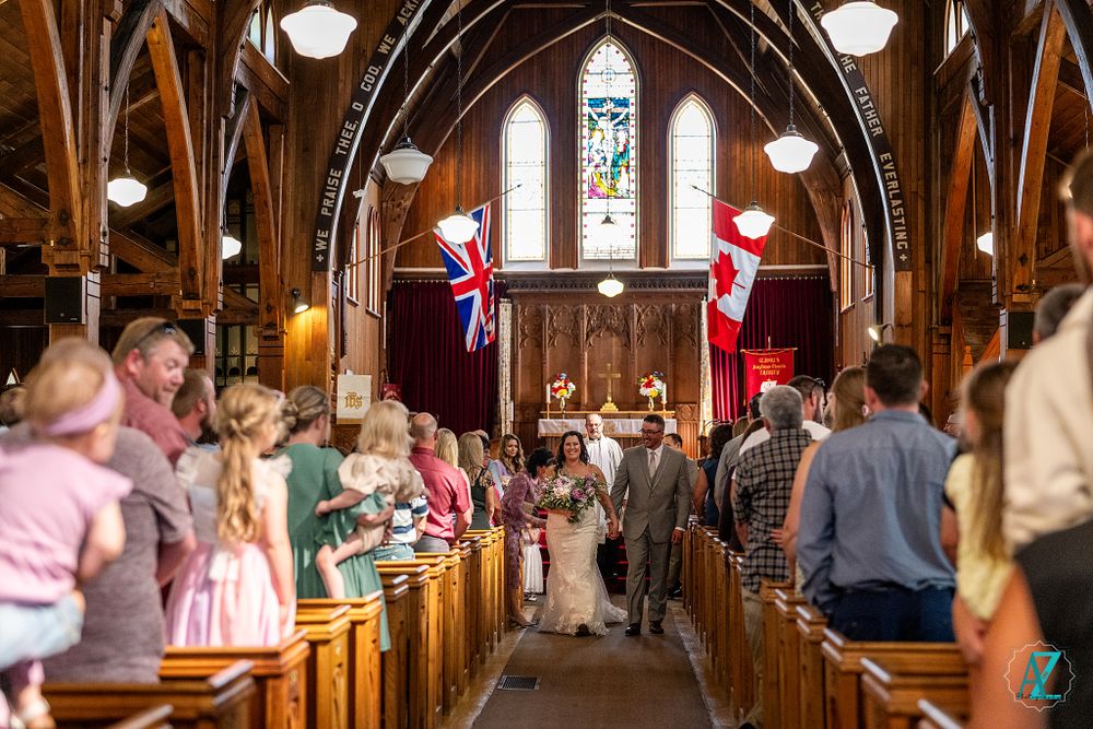 Guests watch as wedding party walks down the aisle in a gothic-style church with flags.
