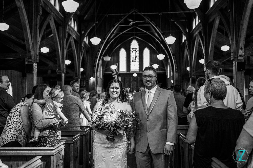 Black and white photo of wedding ceremony inside historic church with dramatic wooden beams.