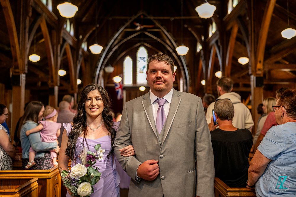 Couple stands in church aisle during wedding ceremony beneath arched wooden beams.