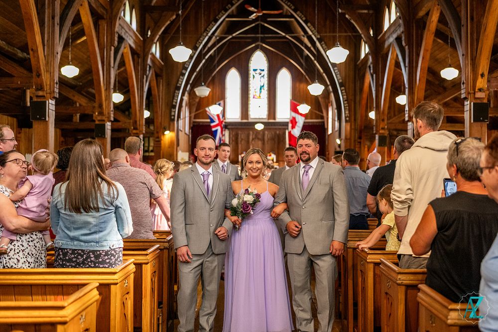 Wedding party poses in center aisle of historic church with dramatic wooden architecture.